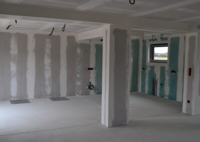 Maison neuve en cours de construction avec pose de cloisons en placo et isolation thermique. Installation de plaques de plâtre sur ossature métallique pour un projet résidentiel.