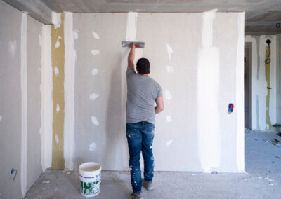 Maison neuve en cours de construction avec pose de cloisons en placo et isolation thermique. Installation de plaques de plâtre sur ossature métallique pour un projet résidentiel.